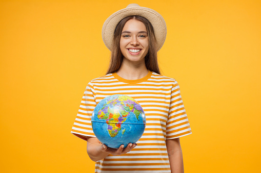 Smiling European woman holding globe on hands isolated on yellow background, concept of travelling