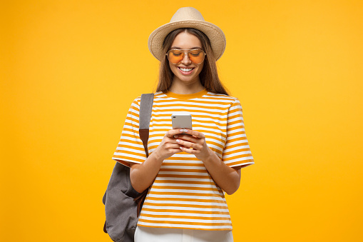Positive Caucasian girl isolated on yellow background browsing pages in her smartphone ready to travel