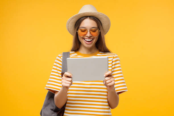 european tourist girl dressed in summer clothes pictured isolated on yellow background with tablet computer in hands - travel ipad isolated backpack imagens e fotografias de stock