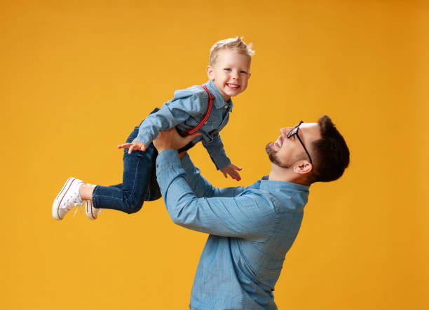 istock happy father's day! cute dad and son hugging on yellow background 1150231910