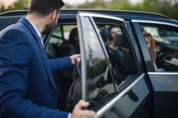 Young man in suit holding bag and getting in the car with his friends. Going on  a road trip.