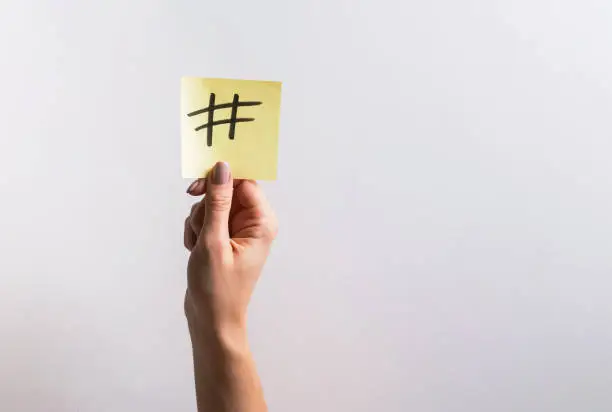 Photo of Woman's hand holding small paper with drawn hashtag symbol on it