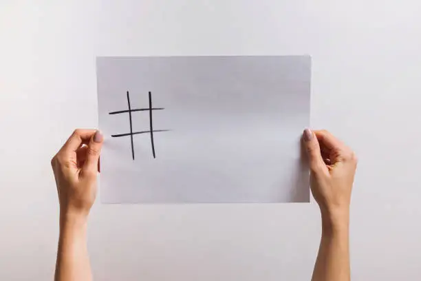 Photo of Woman's hands holding a paper with drawn hashtag symbol and some copy space on it