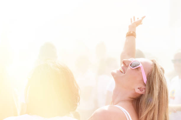 Woman loving the music concert, laughing and dancing with hand raised in the middle of the crowd.