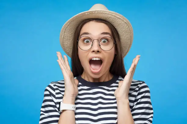 Portrait of shocked young woman, looking at camera with mouth wide open, wearing hat. Oh my god! Wow!