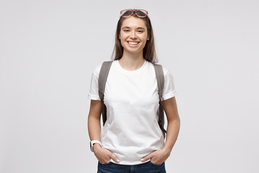 Smiling girl wearing white t-shirt and backpack, isolated on gray background