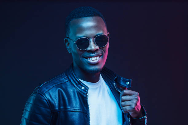 istock African American guy dressed in black leather jacket smiling and looking through black glasses in studio with neon light 1150254176