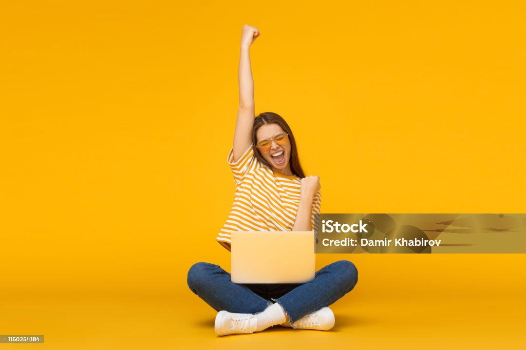 She is a winner! Excited young female with laptop isolated on yellow background Happiness Stock Photo