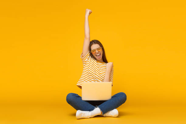 ona jest zwycięzcą! podekscytowana młoda kobieta z laptopem odizolowanym na żółtym tle - winning success women victory zdjęcia i obrazy z banku zdjęć