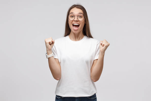 young excited female shouting to support her favorite team or winning lottery, isolated on gray background - women standing fist success imagens e fotografias de stock