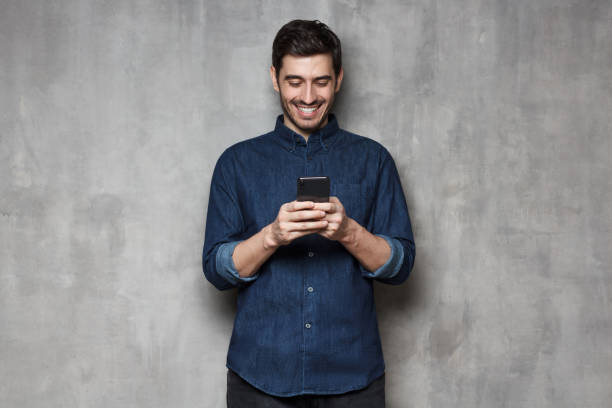 istock Young man smiling and laughing as he is browsing Internet or communicating via phone, isolated on gray textured wall 1150254222