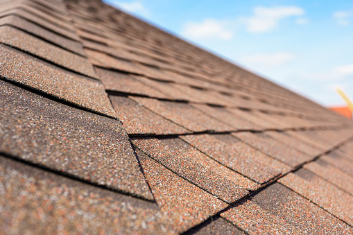 Close up and selective focus photo of asphalt shingle or tile on roof of new house under construction against blue sky