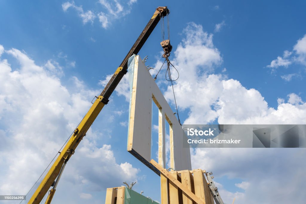 Process of crane construction of new and modern modular house from composite sip panels against background with beautiful blue sky Prefabricated Building Stock Photo