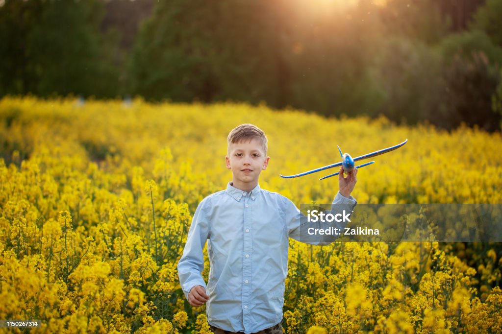 Adorable Boy holds toy plane in his hand on sunset in summer day. Cute Boy holds toy plane in his hand on sunset in summer day. Adventure Stock Photo