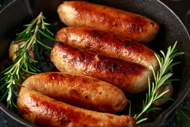 Photo of Freshly cooked butchers made, homemade sausages with rosemary in cast iron frying pan.