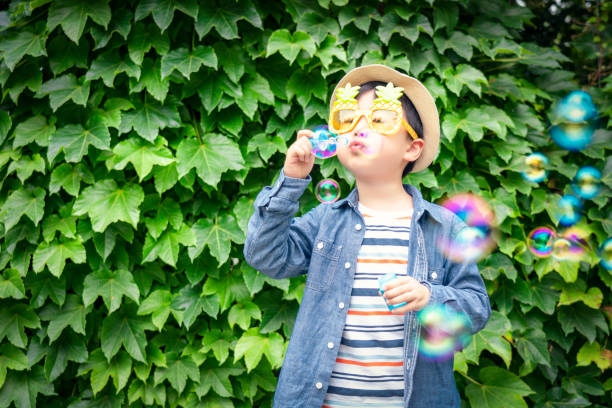 幸せな小さなアジアの男の子が遊び場で泡を吹く - bubble wand child blowing asian ethnicity ストックフォトと画像