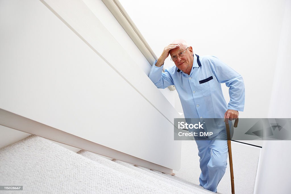 Elderly Man Walking Up a Set of Stairs A senior male patient with a cane is at the bottom of the stairs and looking up at an insurmountable climb. Horizontal shot. Staircase Stock Photo