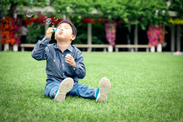 幸せな小さなアジアの男の子が草の上に泡を吹く - bubble wand child blowing asian ethnicity ストックフォトと画像