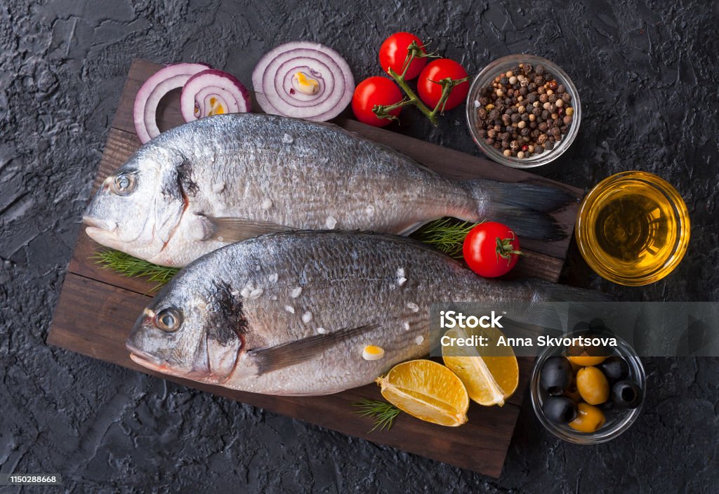 신선한도 라도 생선 요리에 대 한 원시도 라도 생선과 재료 신선한도 라도 생선 소금 토마토 올리브가 나무 보드 위에 있습니다 ...