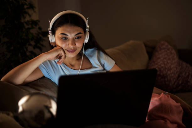 mujer soltera viendo televisión en línea en la noche sentada en un sofá en la sala de estar en casa - attractive female only young women music living room fotografías e imágenes de stock