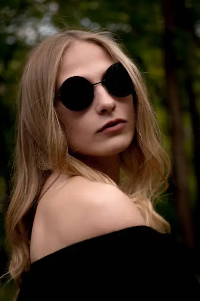A stylish, young blonde woman wearing black sunglasses and dress.