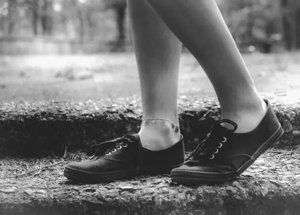 Greyscale image of the bare legs of a person walking outdoors in a park or garden wearing casual lace up sneakers in a close up low angle view