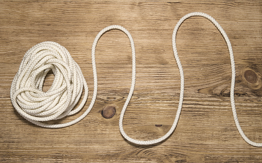 Unwinding hank of white rope on the wooden background. Solving problems business concept.