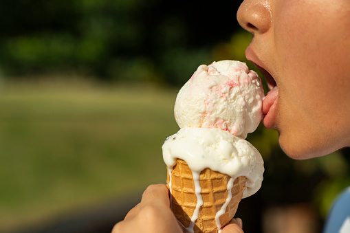 Young asian girl licking a vanilla strawberry ice-cream cone on a bright sunny day