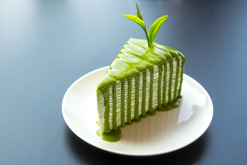 Piece of green tea crape cake on white plate and decorated with fresh tea leaf
