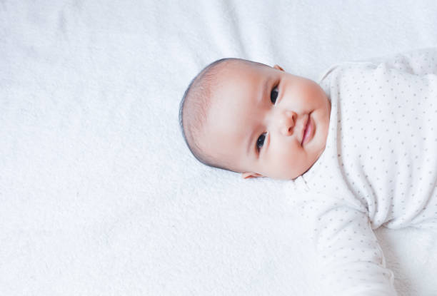 a menina asiática do bebé estabelece na folha de cama branca com pouco sorriso. - newborn little girls baby lying down - fotografias e filmes do acervo