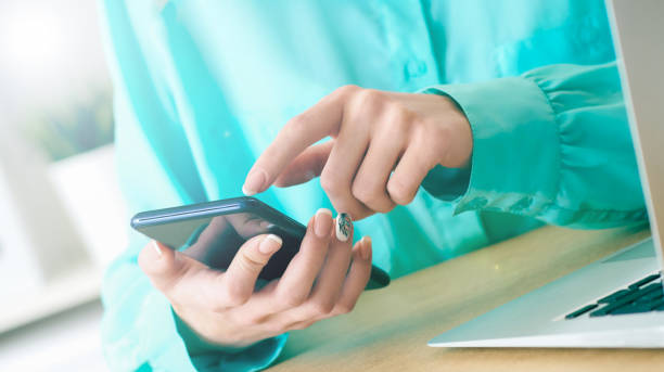 istock Young woman using smartphone for surfing and browsing Internet, searching for required information, sitting at desk with laptop. 1150307745