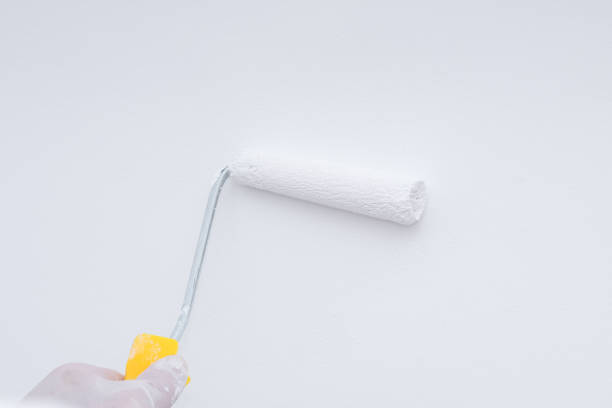 istock Closeup paint roller in hand with white paint on clean wall 1150309591