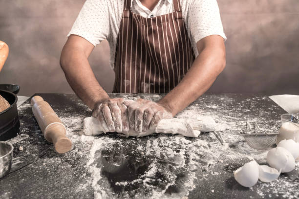 istock Man preparing buns at table in bakery, Man sprinkling flour over fresh dough on kitchen table 1150311059