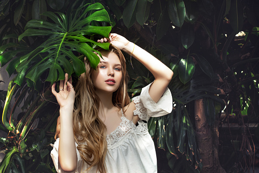Young beautiful happy blonde girl model on tropical plants background with green leaf