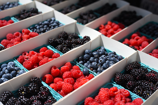 Raspberries, blueberries, and blackberries in small containers on display at a farmer's market for sale.
