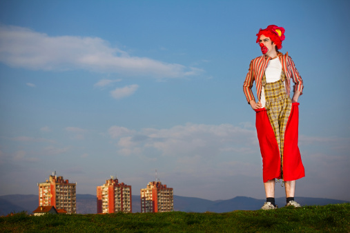 Clown standing at the top of the hill with three buildings peeking from behind.