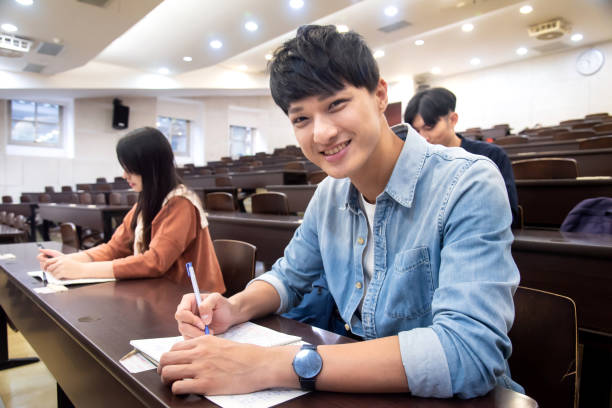 Young male student smiling and showed confidence in his study Students listening to lecture and taking notes in auditorium male chinese student stock pictures, royalty-free photos & images