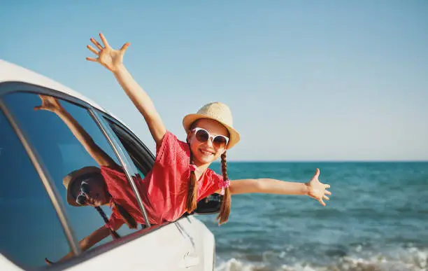 Photo of happy child girl goes to summer travel trip in car