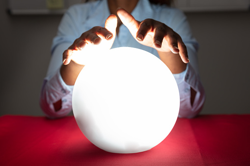 Close-up Of Fortuneteller's Hand Covering The Glowing Crystal Ball On Red Desk