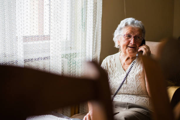 mujer senior positiva hablando por teléfono - one person lifestyles 80 plus years indoors fotografías e imágenes de stock