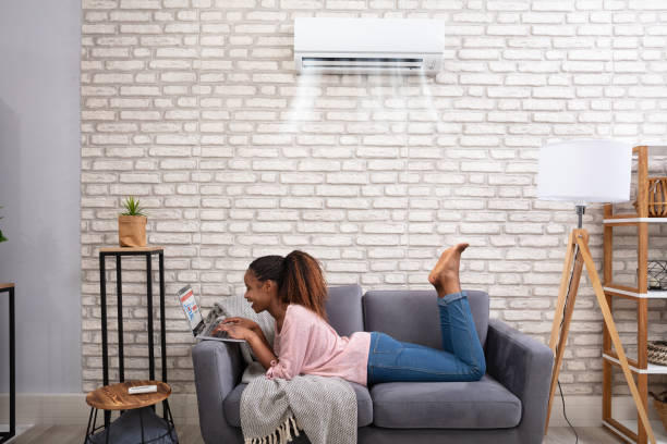 femme utilisant l’ordinateur portatif appréciant le refroidissement sous l’air conditionné - air conditioner photos et images de collection