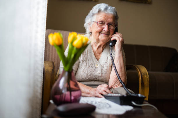 Happy senior woman talking on the phone in living room. Old woman with gray white hair and glasses sitting in her armchair in her home and talking on the phone. Grandmother is happy to talk to her children and grandchildren. only senior women stock pictures, royalty-free photos & images