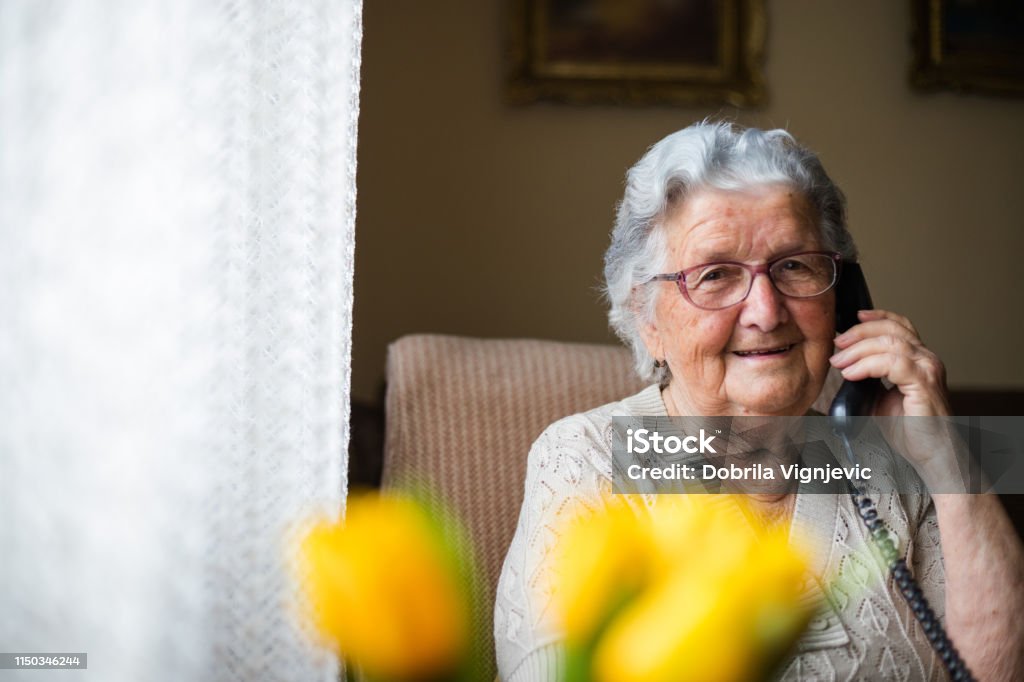 Portrait of an older woman talking with the phone. Old senior woman having a cheerful conversation over her phone, talking with a friend or a relative . Senior Adult Stock Photo