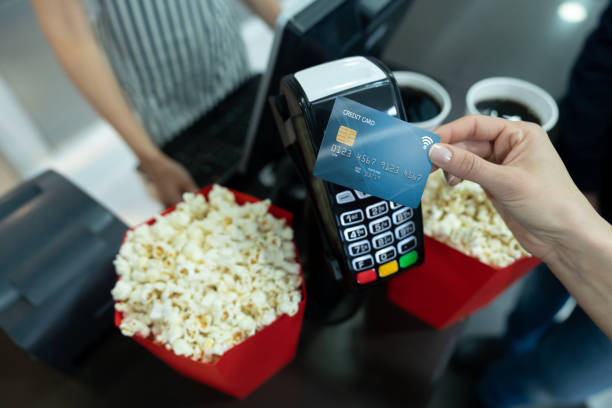 Buying popcorn at the cinema and making a contactless payment Close-up on a customer buying popcorn at the cinema and making a contactless payment. **DESIGN ON CREDIT CARD WAS MADE FROM SCRATCH BY US** concession stand stock pictures, royalty-free photos & images