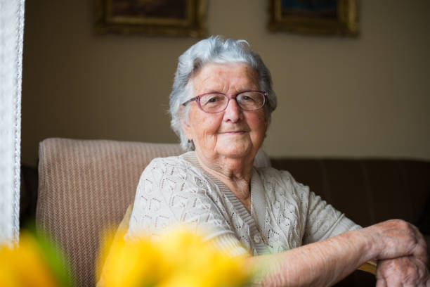 Close-up portrait of happy senior woman portrait Portrait of a beautiful old woman with gray hair and glasses is sitting in a chair in her home. nostalgia 80s stock pictures, royalty-free photos & images