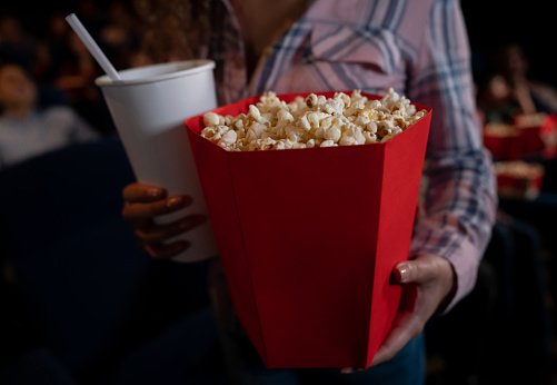 Close-up on a woman having popcorn and soda for a snack at the movies - food and drinks concepts