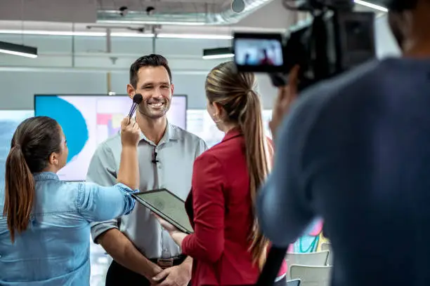 Happy businessman during corporate interview with journalist. Vip or manager talking and smiling in office. Woman at work as makeup artist with business man and cameraman shooting video with camera