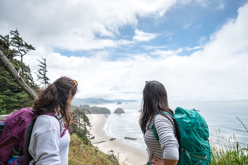 Eurasian sisters hiking along coastal bluff trail, Ecola State Park, Oregon, USA.  Cannon Beach in the background.