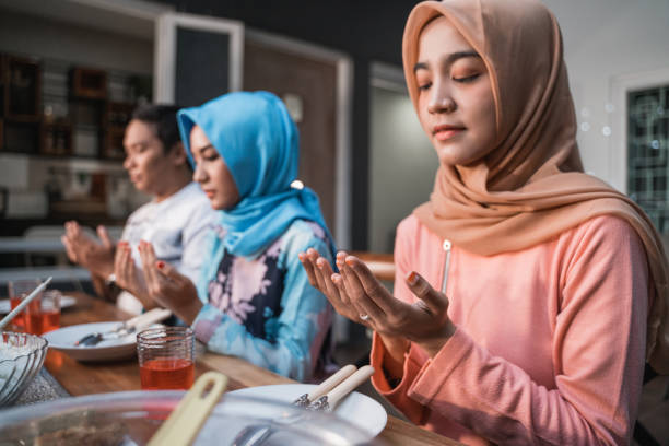 Hijab women and a man pray together before meals Hijab women and a man pray together before meals, a fast breaking meal served on a table in backyard eid ul fitr photos stock pictures, royalty-free photos & images