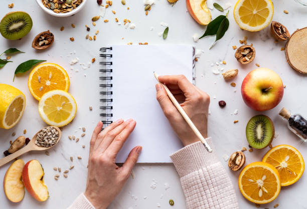 a mão fêmea escreve no caderno no fundo saudável do alimento, menu da receita da nutrição da dieta das mulheres, sementes frescas do granola do fruto do verão na tabela branca alimento super orgânico, detox dos cuidados médicos, vista superior, esp - granola breakfast dieting food - fotografias e filmes do acervo